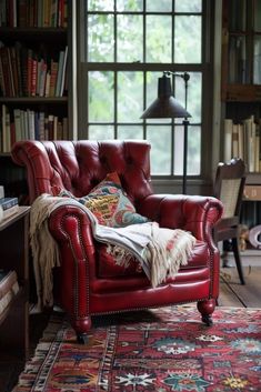 a red leather chair sitting in front of a book shelf filled with books and pillows