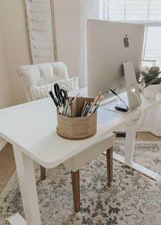 an apple computer sitting on top of a white desk next to a chair and window