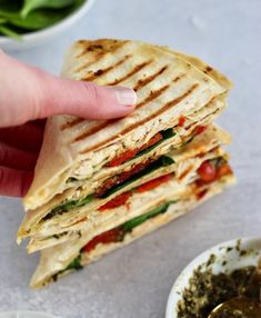 a hand holding a sandwich over a white plate with some other food on the table