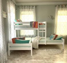 two white bunk beds sitting next to each other in a room with curtains on the windows