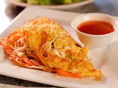 an omelet on a white plate with dipping sauce in a bowl next to it