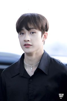 the young man is wearing a black shirt and silver choker on his neck, looking at the camera