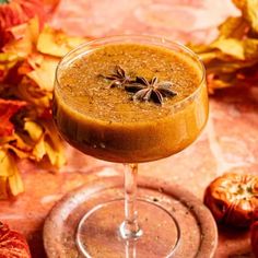 a close up of a drink in a wine glass on a table with autumn leaves