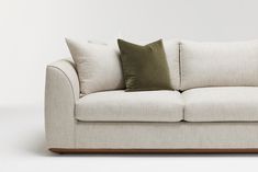 a white couch with two green pillows on it's back and one brown pillow