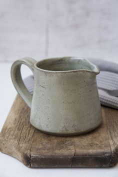 a white ceramic pitcher sitting on top of a wooden board next to a gray hat