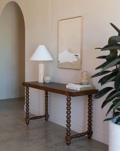 a wooden table sitting next to a plant and a white lamp on top of it