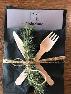 a fork and knife wrapped in twine on top of a black napkin with a green sprig