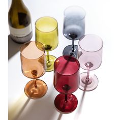 several different colored wine glasses sitting next to each other in front of a white background