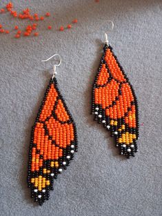 two orange and black beaded earrings sitting on top of a gray surface next to beads