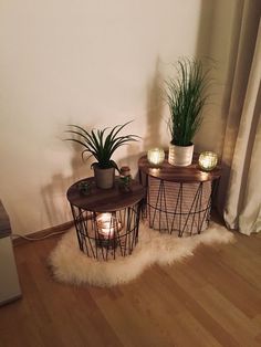 two small tables with plants on them in front of a white wall and wooden floor