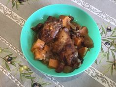 a blue bowl filled with meat and vegetables on top of a tablecloth covered table