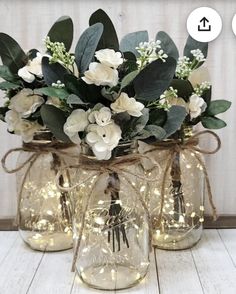 three mason jars with flowers and lights in them