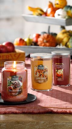 three candles sitting on top of a table next to apples and other fruit in the background