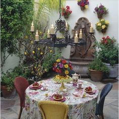 a dining table with flowers and candles on it in front of an outdoor wall decoration