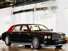 a black and red car parked in front of a white building with glass walls behind it