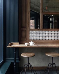 two stools sit in front of a counter with a tea cup on it next to a mirror