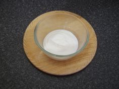 a glass bowl filled with yogurt sitting on top of a wooden plate next to a black counter