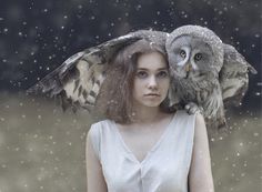 a woman with an owl on her shoulder standing in the snow while it's raining