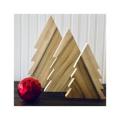 three wooden christmas trees on a table with a red ornament next to them