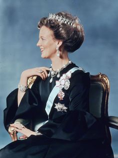 an old photo of a woman in a black dress and tiara sitting on a chair