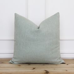 a light green pillow sitting on top of a wooden floor next to a white wall