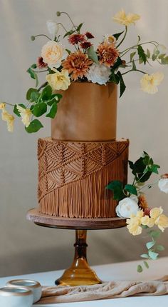 a three tiered cake decorated with flowers and greenery on a wooden stand in front of a wall