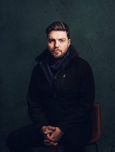 a man sitting in a chair with his hands on his knees and looking at the camera