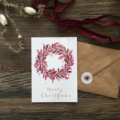 a christmas card with a wreath on it next to a brown envelope and red ribbon