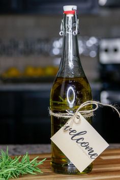 a bottle of olive oil with a tag on it sitting on a cutting board next to a sprig of rosemary