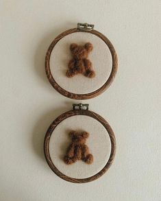 two cross stitch teddy bears are hanging on the wall in small hoops, one is brown and the other is white