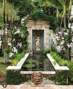 an outdoor fountain surrounded by flowers and greenery in the middle of a garden area