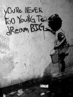 a black and white photo with graffiti on the side of a wall that says, you're never too young to dream big