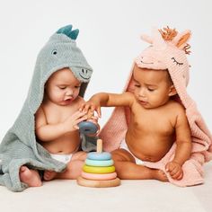 two babies sitting on the floor playing with toys and blankets over their heads, one holding a toy