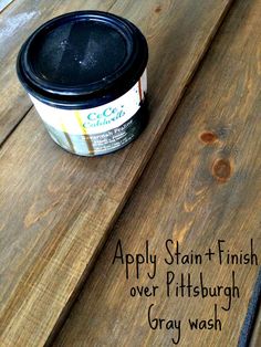 a can of paint sitting on top of a wooden table next to a black brush