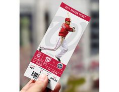 a person holding up a baseball ticket with the image of a player in red and white