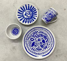 three blue and white plates sitting next to each other on a cement surface with two cups in the middle