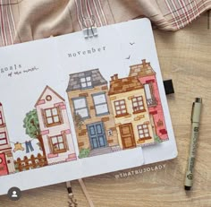 an open notebook with houses drawn on it next to a marker and pen, along with other items