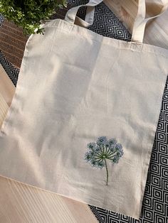 a white tote bag with a blue flower embroidered on the front and side, sitting on a wooden surface