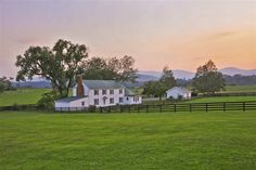 a large white house sitting on top of a lush green field next to a fence