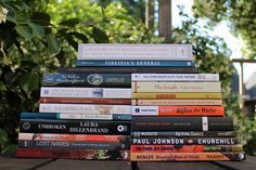 a stack of books sitting on top of a wooden table in front of trees and bushes