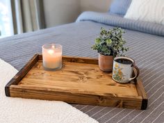 a wooden tray with a candle and potted plant on it sitting on a bed