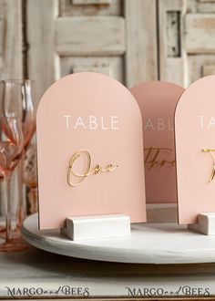 two place cards are on a plate with wine glasses in front of them and the table name is gold