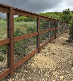 a wooden fence on the side of a dirt road with rocks and grass around it