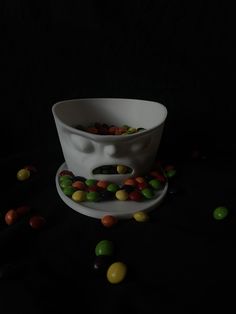 a white bowl filled with candy beans on top of a black table next to other candies