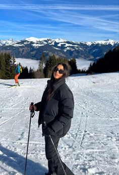 a woman standing on top of a snow covered slope wearing skis and holding ski poles