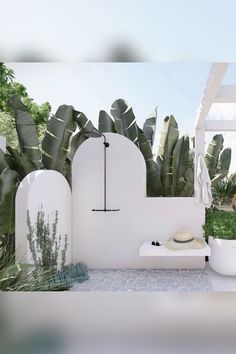 an outdoor shower with plants and a hat on the bench next to it in front of a white wall