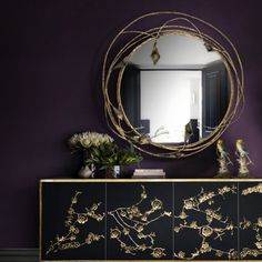 a black and gold sideboard against a purple wall with a round mirror above it