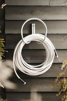 a white extension cord attached to a wooden wall next to a potted plant on the side of a house