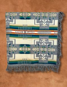 a blanket with fringes on top of a brown floor in front of a tan wall