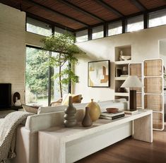 a living room filled with furniture next to a large glass window and a tree in the corner